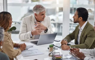 Businessman with laptop and team with documents in meeting for strategy planning at office