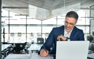 smiling man sitting at desk in front of laptop computer